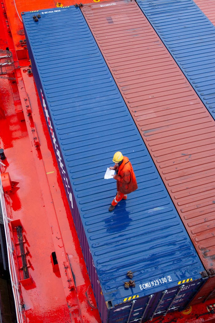 services-03 Overhead view of a worker inspecting containers on a ship deck in a maritime setting.