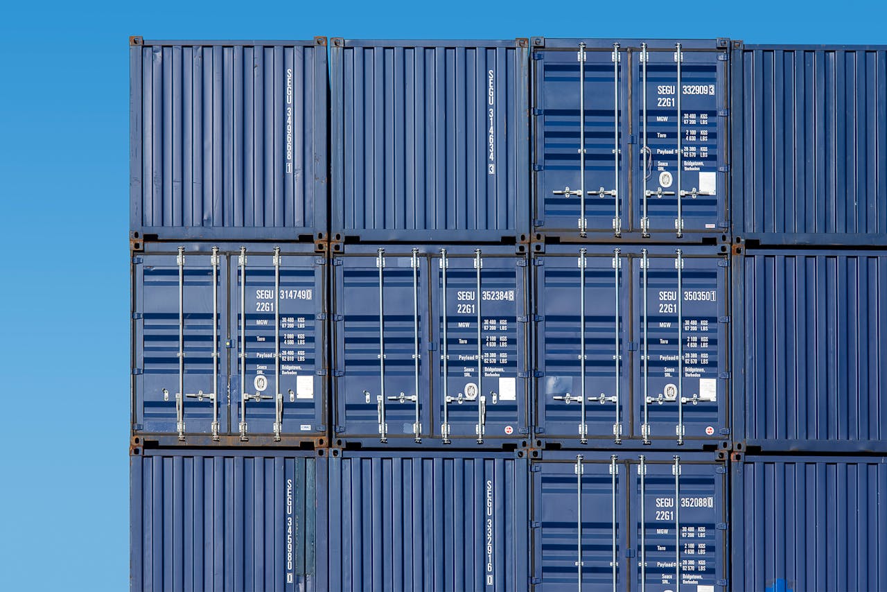 Close-up of blue shipping containers stacked high at Rotterdam Port under a clear blue sky.